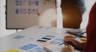 A person writing in a notebook on a table cover with wireframe designs.
